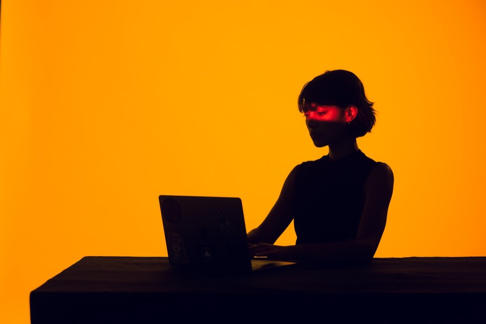 silhouette of a person working at a laptop against an orange background